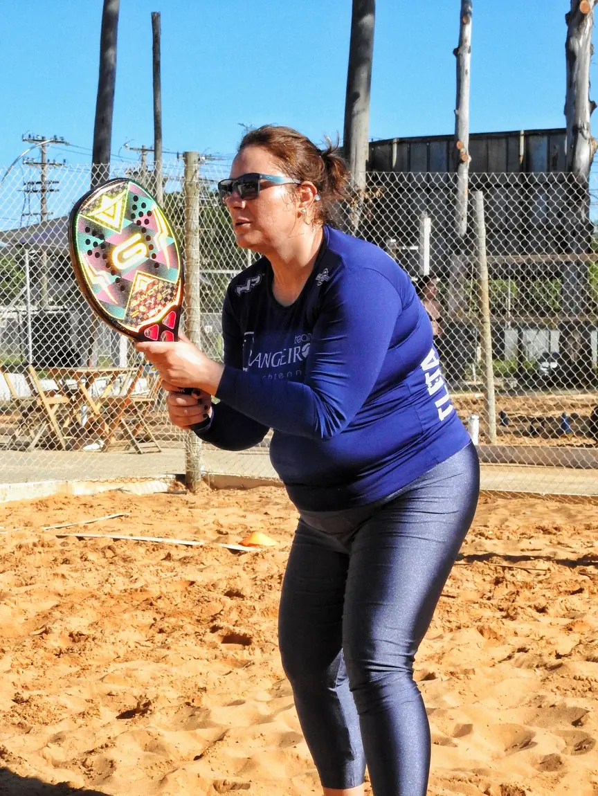 Aluna posicionada para devolver a bola em treino de beach tennis