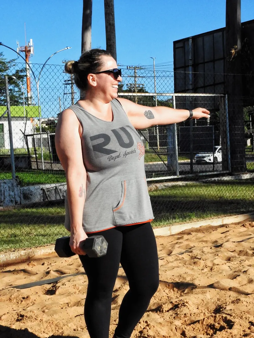 Aluna em treino funcional na areia com peso na mão